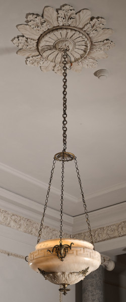 Ampla alabastrowa. Dekorowana mosiężnymi łbami kozłów misa wisząca na łańcuchach. Całość na jednym łańcuchu zamocowana do sufitu.