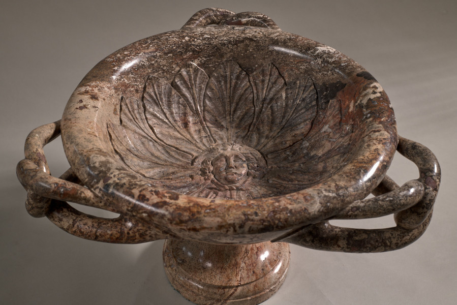 Waza z ciemnego marmuru z trzema splecionymi uchwytami. Waza spoczywa na trzonie z okrągłą stopą. Wewnątrz czary rzeźbiona głowa Meduzy.