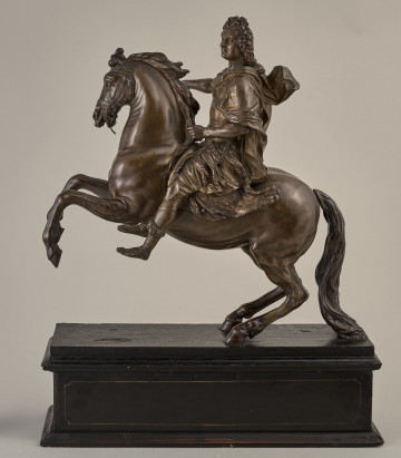 Brązowy posążek na drewnianym postumencie przedstawia Ludwika XIV siedzącego na wspiętym koniu, w stroju i pozie rzymskiego imperatora, w peruce na głowie.