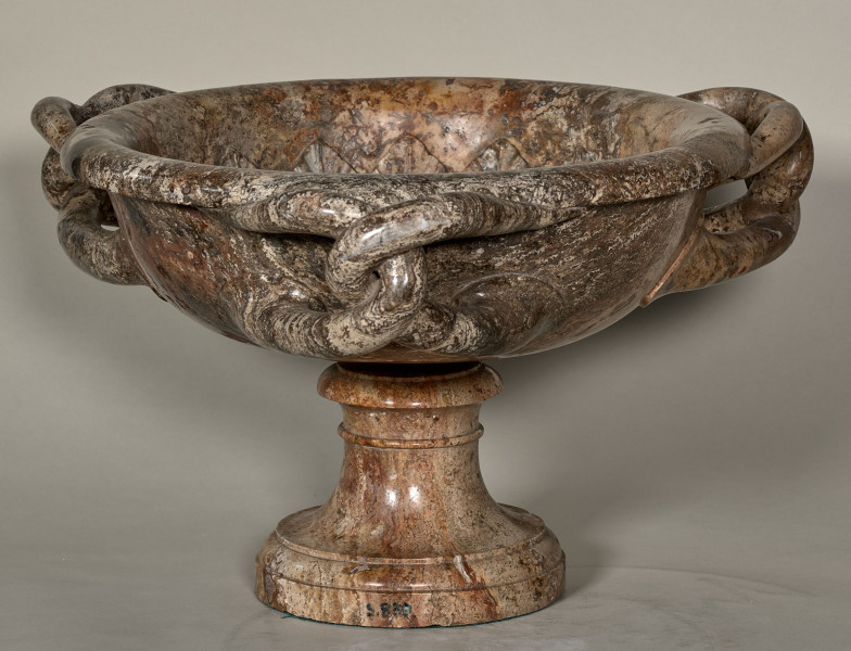 Waza z ciemnego marmuru z trzema splecionymi uchwytami. Waza spoczywa na trzonie z okrągłą stopą. Wewnątrz czary rzeźbiona głowa Meduzy.