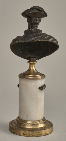 Henryk IV. Brązowe, miniaturowe popiersie przedstawia starszego mężczyznę o szczupłej twarzy, wydatnym nosie, z wąsami i brodą. W kapeluszu z piórami. Ubrany jest w kaftan z wąską krezą i w płaszcz lamowany futrem, na którym widnieje krzyż orderowy. Popiersie ustawione jest na podstawie złożonej z mosiężnego cokoliku, marmurowego trzonu ujętego metalowym łańcuszkiem i mosiężnej bazy. Tył