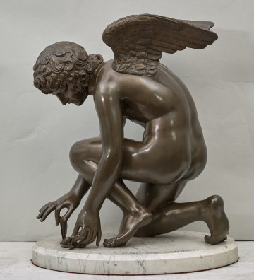 Amorek bawiący się motylem. Brązowy posążek przykucniętej postaci amorka skrzydlatego bawiącego się małym motylkiem. Postać amorka na marmurowej podstawie. Bok lewy