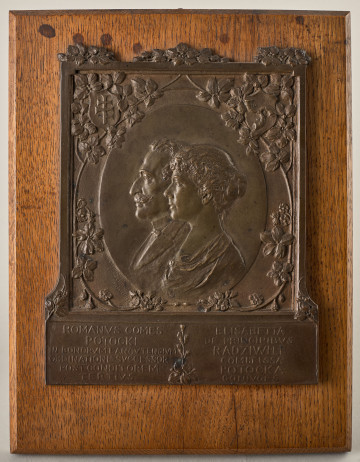 Plakietka płaskorzeźbiona z brązu przedstawiająca Romana i Elżbietę Potockich. Płaskorzeźba zamocowana na drewnianym podkładzie.