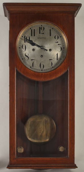 Zegar szafkowy, wiszący ma kształt prostopadłościanu z gzymsem i profilowanym cokołem. W dolnej części jest przeszklony, dzięki czemu widać wahadło zakończone dużym, metalowym kołem. Na metalowej, okrągłej tarczy umieszczono cyfry arabskie i napis: MARTIN HALBKRAM / K. u. K HOF.UHRMACHER / WIEN I