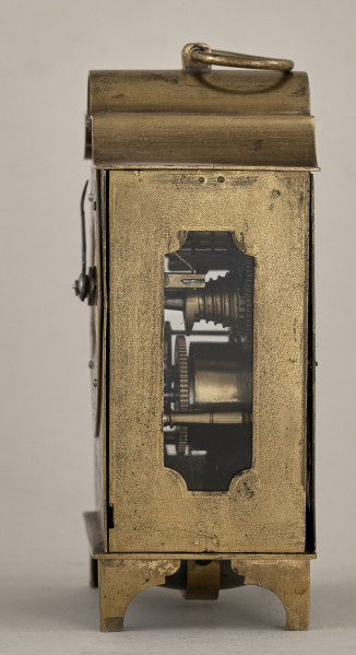 Boczna, złocona ścianka zegara ze szklonym otworem ukazującym mechanizm.