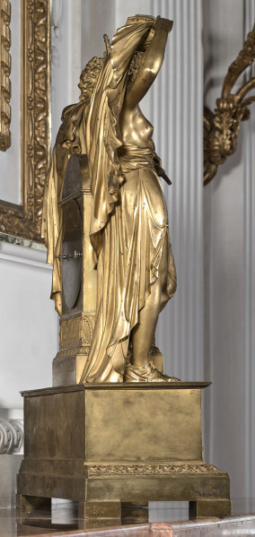 Zegar kominkowy wykonany z brązu złoconego, którego dekoracyjna obudowa przedstawia postaci mitologiczne Dianę trzymającą łuk i Apollina z lirą opartych na prostopadłościennej obudowie werku, która została umieszczona na postumencie w typie sarkofagu, wspartym na czterech prostopadłościennych nóżkach. Bok lewy od tylnej strony.