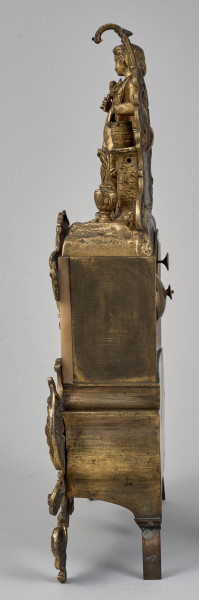 ﻿Zegar kominkowy wykonany z brązu, wsparty na czterech nóżkach, bogato dekorowany. Boczna ścianka zegara.