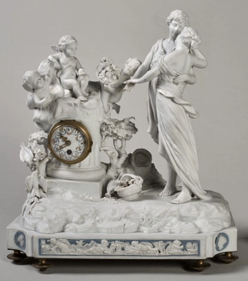 ﻿Prezentowany zegar został wykonany z biskwitowej porcelany twardej, w pełnoplastycznej oprawie rzeźby figuralnej. Tematem jest para młodych pasterzy zapatrzonych w siebie ujęta w ruchu tanecznym. Kierują się w stronę ściętej kolumny, a na jej szczycie siedzą trzy uskrzydlone amorki, z których jeden trzyma w dłoniach róg obfitości. Ponadto u stóp pasterzy znajduje się, laska, kapelusz, dzban i koszyk. Dopełnieniem sceny są dwa gołąbki i konary krzewów. Stroje postaci nawiązują do antyku. Mechanizm zegara został wmontowany w kolumnę. Na białej tarczy cyfry rzymskie wskazujące godziny. Podłoże nawiazuje do ziemi pokrytej roślinnością. Ujęcie frontalne
