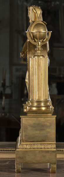 Bok zegara kominkowego, złoconego, o dwóch poziomach kompozycji. Podstawa na nóżkach, z pasem kimationu. Powyżej kolumna z globusem i ulistnioną gałęzią.