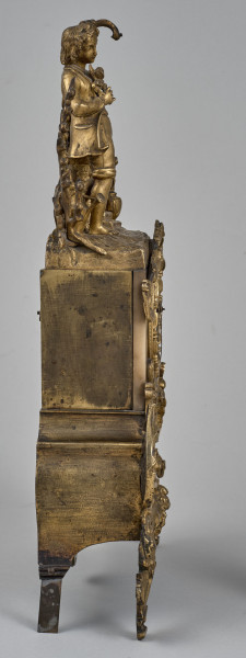 Zegar kominkowy wykonany z brązu, wsparty na czterech nóżkach, bogato dekorowany. Boczna ścianka zegara.