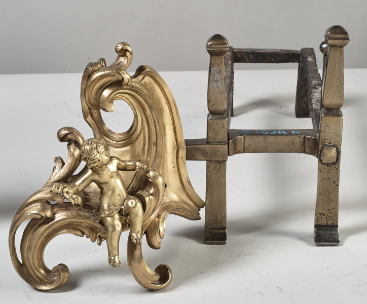 Wilki kominkowe. Ruszt z numerem inwentarzowym i część dekoracyjna w formie dużego rocaila z siedzącym puttem