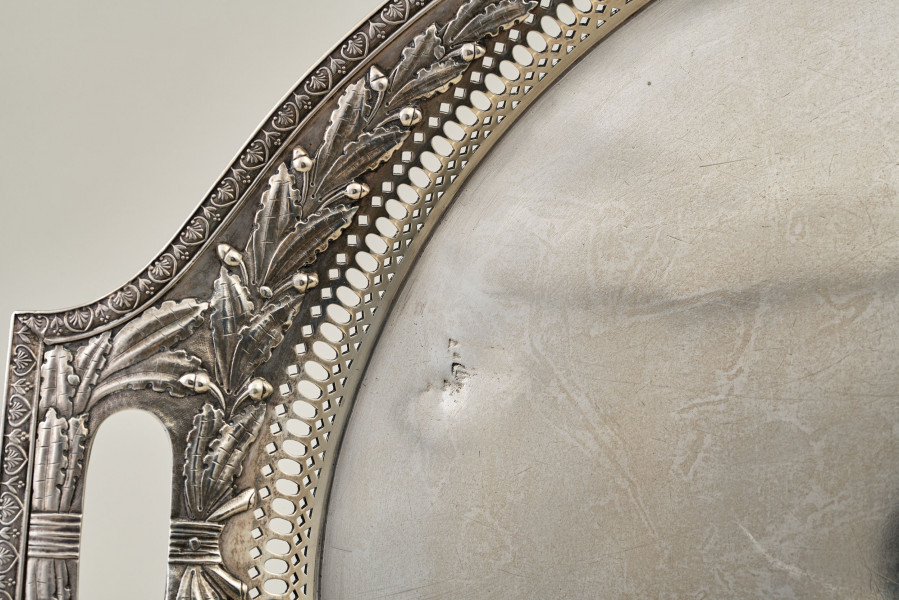 Srebrna taca. Fragment z widocznym lewym uchwytem i dekoracją roślinną brzegu.