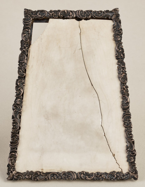 Ramka na menu. Ramka srebrna dekorowana ornamentem roślinnym.Wewnątrz płytka ceramiczna, pęknięta pionowo.