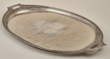 Taca srebrna, owalna z dekoracyjnym brzegiem z dwoma uchwytami. Taca w ujęciu bocznym leżąca płasko.