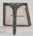 Ramka na menu. Ramka srebrna dekorowana ornamentem roślinnym.Wewnątrz płytka ceramiczna, pęknięta pionowo. Widok od tyłu z widoczną podpórką.