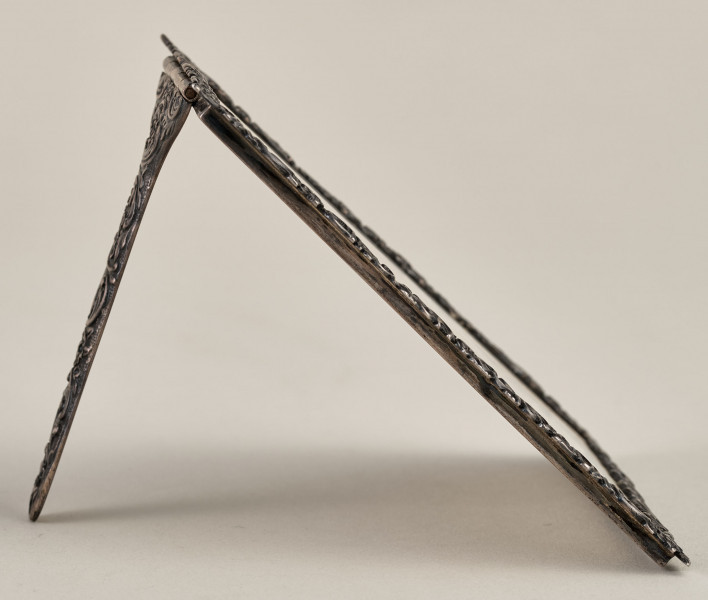 Ramka na menu. Ramka srebrna dekorowana ornamentem roślinnym. Ujęcie boczne z widoczną podpórką.