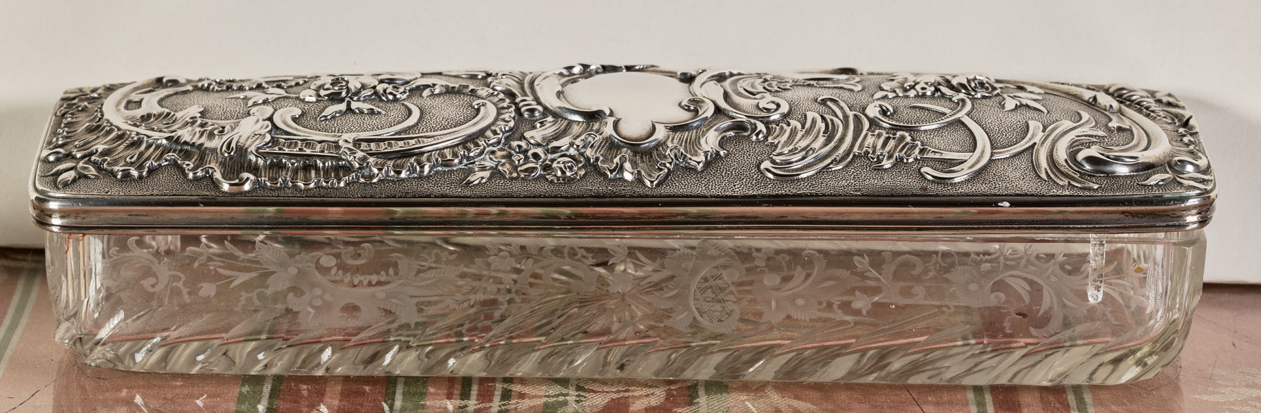 ﻿Kasetka ze szkła kryształowego i srebra. Ujęcie od strony szerszej. Pokrywa srebrna bogato dekorowana.