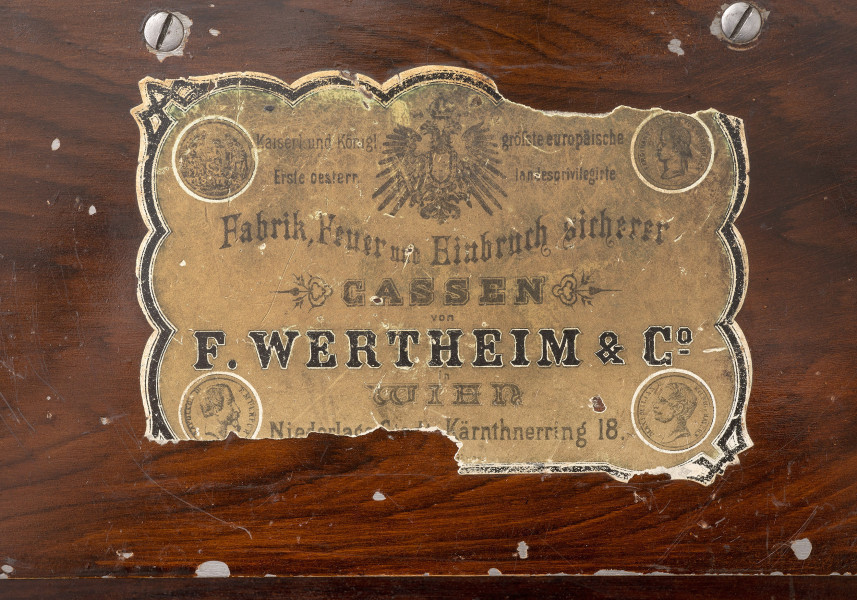 papierowa etykieta firmowa na osłonie mechanizmu zamka, na spodniej stronie wieka