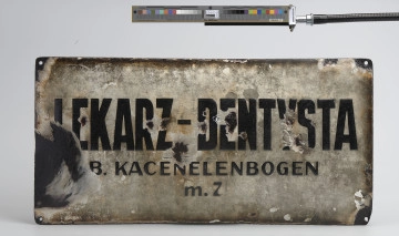 Ujęcie przodu. Blaszany, emaliowany szyld praktyki dentystycznej z getta warszawskiego.
