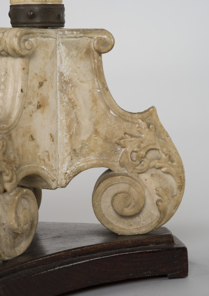 zbliżenie na trójdzielną, kamienną podstawę z wolutami, umieszczoną na drewnianym, profilowanym cokole