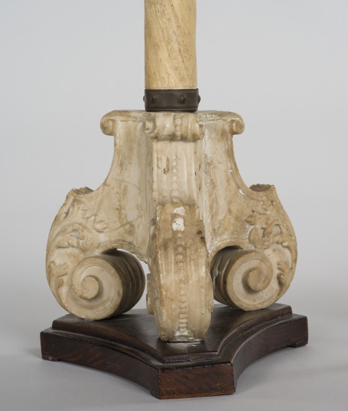 zbliżenie na trójdzielną, kamienną podstawę z wolutami, umieszczoną na drewnianym, profilowanym cokole