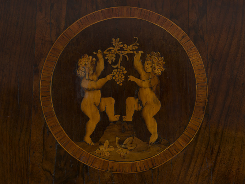 zbliżenie na intarsjowaną dekorację blatu w formie medalionu z dwoma puttami trzymającymi pęd winorośli