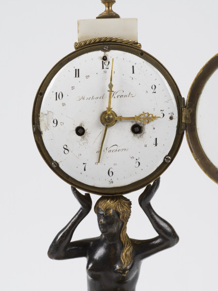 zbliżenie na białą, emaliowaną tarczę zegara oraz mosiężne wskazówki