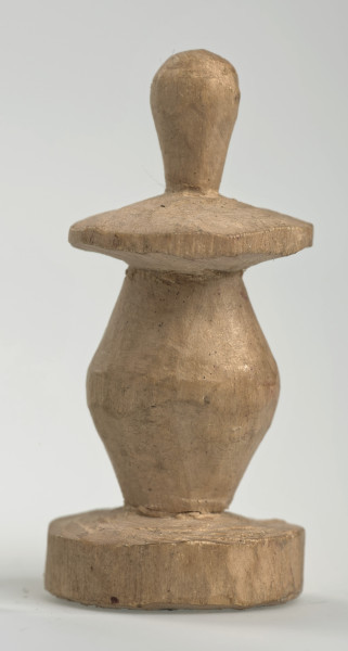 Ujęcie z boku [3]. Ze względu na swój okrągły kształt kolejne ujęcia z boku nie różnią się między sobą znacząco. Pionek został wykonany ręcznie z jednego kawałka jasnego drewna. Na całej powierzchni widoczne są ślady rzeźbienia przy pomocy noża. Obiekt w kolorze naturalnego drewna (nie został pomalowany, ani polakierowany). Od spodu widoczne oznaczenie składające się z dwóch przecinających się ze sobą linii („X”), które umożliwia podzielenie bierek pomiędzy dwóch graczy - wszystkie bierki są jednakowego koloru. Krawędź podstawy została dodatkowo obrysowana ołówkiem. Pionek składa się ze spłaszczonej podstawy w formie krążka, części środkowej w kształcie gruszki, spłaszczonego ronda, które zwęża się stopniowo ku górze oraz ku dołowi (przypominając dwa połączone ze sobą talerze, z których każdy skierowany jest dnem do zewnątrz) oraz zwieńczenia o prostej, rozszerzającej się ku górze formie (przypominającej pałkę).