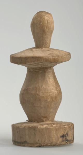 Ujęcie z boku [4]. Ze względu na swój okrągły kształt kolejne ujęcia z boku nie różnią się między sobą znacząco. Pionek został wykonany ręcznie z jednego kawałka jasnego drewna. Na całej powierzchni widoczne są ślady rzeźbienia przy pomocy noża. Obiekt w kolorze naturalnego drewna (nie został pomalowany, ani polakierowany). Krawędź podstawy została dodatkowo obrysowana ołówkiem. Pionek składa się ze spłaszczonej podstawy w formie krążka, części środkowej w kształcie gruszki, spłaszczonego ronda, które zwęża się stopniowo ku górze oraz ku dołowi (przypominając dwa połączone ze sobą talerze, z których każdy skierowany jest dnem do zewnątrz) oraz zwieńczenia o prostej, rozszerzającej się ku górze formie (przypominającej pałkę).