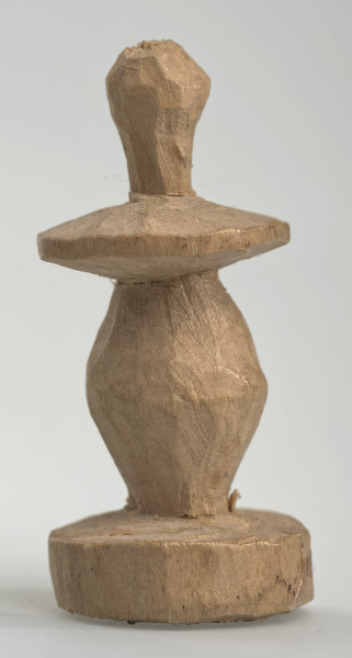 Ujęcie z boku [4]. Ze względu na swój okrągły kształt kolejne ujęcia z boku nie różnią się między sobą znacząco. Pionek został wykonany ręcznie z jednego kawałka jasnego drewna. Na całej powierzchni widoczne są ślady rzeźbienia przy pomocy noża. Obiekt w kolorze naturalnego drewna (nie został pomalowany, ani polakierowany). Od spodu widoczne oznaczenie składające się z dwóch przecinających się ze sobą linii („X”), które umożliwia podzielenie bierek pomiędzy dwóch graczy - wszystkie bierki są jednakowego koloru. Krawędź podstawy została dodatkowo obrysowana ołówkiem. Pionek składa się ze spłaszczonej podstawy w formie krążka, części środkowej w kształcie gruszki, spłaszczonego ronda, które zwęża się stopniowo ku górze oraz ku dołowi (przypominając dwa połączone ze sobą talerze, z których każdy skierowany jest dnem do zewnątrz) oraz zwieńczenia o prostej, rozszerzającej się ku górze formie (przypominającej pałkę).