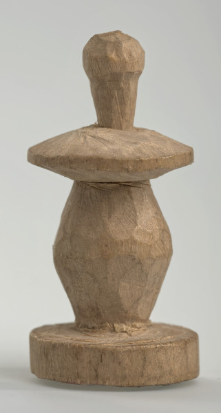 Ujęcie z boku [2]. Ze względu na swój okrągły kształt kolejne ujęcia z boku nie różnią się między sobą znacząco. Pionek został wykonany ręcznie z jednego kawałka jasnego drewna. Na całej powierzchni widoczne są ślady rzeźbienia przy pomocy noża. Obiekt w kolorze naturalnego drewna (nie został pomalowany, ani polakierowany). Krawędź podstawy została dodatkowo obrysowana ołówkiem. Pionek składa się ze spłaszczonej podstawy w formie krążka, części środkowej w kształcie gruszki, spłaszczonego ronda, które zwęża się stopniowo ku górze oraz ku dołowi (przypominając dwa połączone ze sobą talerze, z których każdy skierowany jest dnem do zewnątrz) oraz zwieńczenia o prostej, rozszerzającej się ku górze formie (przypominającej pałkę).