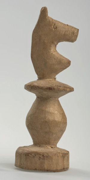 Ujęcie prawego boku. 
Skoczek został wykonany ręcznie z jednego kawałka jasnego drewna. Na całej powierzchni widoczne są ślady rzeźbienia przy pomocy noża. Obiekt w kolorze naturalnego drewna (nie został pomalowany, ani polakierowany). Krawędź podstawy została dodatkowo obrysowana ołówkiem. Skoczek składa się ze spłaszczonej podstawy w formie krążka, części środkowej w formie walca rozszerzającego się po środku wysokości, spłaszczonego cylindrycznego elementu, który zwęża się stopniowo ku górze oraz ku dołowi (przypominając dwa połączone ze sobą talerze, z których każdy skierowany jest dnem do zewnątrz) oraz zwieńczenia w formie nawiązującej do głowy i szyi konia. Głowa oraz szyja są spłaszczone. Widoczne wyżłobione oko.