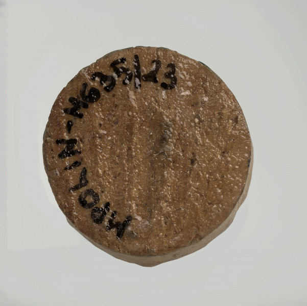 Ujęcie na spód obiektu. Okrągła podstawa skoczka. Ponieważ był on rzeźbiony ręcznie krawędź nie jest idealnie równa. Wzdłuż krawędzi widać czarny numer inwentarzowy MPOLIN-M635/23.