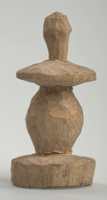 Ujęcie z boku [1]. Ze względu na swój okrągły kształt kolejne ujęcia z boku nie różnią się między sobą znacząco. Pionek został wykonany ręcznie z jednego kawałka jasnego drewna. Na całej powierzchni widoczne są ślady rzeźbienia przy pomocy noża. Obiekt w kolorze naturalnego drewna (nie został pomalowany, ani polakierowany). Krawędź podstawy została dodatkowo obrysowana ołówkiem. Pionek składa się ze spłaszczonej podstawy w formie krążka, części środkowej w kształcie gruszki, spłaszczonego ronda, które zwęża się stopniowo ku górze oraz ku dołowi (przypominając dwa połączone ze sobą talerze, z których każdy skierowany jest dnem do zewnątrz) oraz zwieńczenia o prostej, rozszerzającej się ku górze formie (przypominającej pałkę).