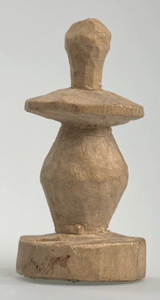 Ujęcie z boku [1]. Ze względu na swój okrągły kształt kolejne ujęcia z boku nie różnią się między sobą znacząco. Pionek został wykonany ręcznie z jednego kawałka jasnego drewna. Na całej powierzchni widoczne są ślady rzeźbienia przy pomocy noża. Obiekt w kolorze naturalnego drewna (nie został pomalowany, ani polakierowany). Od spodu widoczne oznaczenie składające się z dwóch przecinających się ze sobą linii („X”), które umożliwia podzielenie bierek pomiędzy dwóch graczy - wszystkie bierki są jednakowego koloru. Krawędź podstawy została dodatkowo obrysowana ołówkiem. Pionek składa się ze spłaszczonej podstawy w formie krążka, części środkowej w kształcie gruszki, spłaszczonego ronda, które zwęża się stopniowo ku górze oraz ku dołowi (przypominając dwa połączone ze sobą talerze, z których każdy skierowany jest dnem do zewnątrz) oraz zwieńczenia o prostej, rozszerzającej się ku górze formie (przypominającej pałkę).