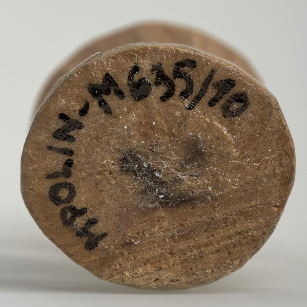 Ujęcie na spód obiektu. Okrągła podstawa pionka szachowego. Ponieważ był on rzeźbiony ręcznie krawędź nie jest idealnie równa. Pośrodku widoczny czarny 