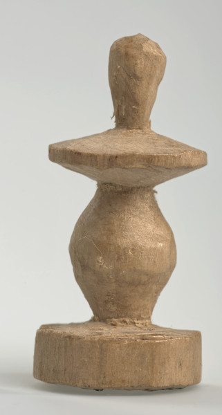 Ujęcie z boku [4]. Ze względu na swój okrągły kształt kolejne ujęcia z boku nie różnią się między sobą znacząco. Pionek został wykonany ręcznie z jednego kawałka jasnego drewna. Na całej powierzchni widoczne są ślady rzeźbienia przy pomocy noża. Obiekt w kolorze naturalnego drewna (nie został pomalowany, ani polakierowany). Od spodu widoczne oznaczenie składające się z dwóch przecinających się ze sobą linii („X”), które umożliwia podzielenie bierek pomiędzy dwóch graczy - wszystkie bierki są jednakowego koloru. Krawędź podstawy została dodatkowo obrysowana ołówkiem. Pionek składa się ze spłaszczonej podstawy w formie krążka, części środkowej w kształcie gruszki, spłaszczonego ronda, które zwęża się stopniowo ku górze oraz ku dołowi (przypominając dwa połączone ze sobą talerze, z których każdy skierowany jest dnem do zewnątrz) oraz zwieńczenia o prostej, rozszerzającej się ku górze formie (przypominającej pałkę).