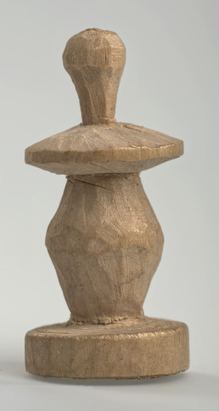 Ujęcie z boku [3]. Ze względu na swój okrągły kształt kolejne ujęcia z boku nie różnią się między sobą znacząco. Pionek został wykonany ręcznie z jednego kawałka jasnego drewna. Na całej powierzchni widoczne są ślady rzeźbienia przy pomocy noża. Obiekt w kolorze naturalnego drewna (nie został pomalowany, ani polakierowany). Krawędź podstawy została dodatkowo obrysowana ołówkiem. Pionek składa się ze spłaszczonej podstawy w formie krążka, części środkowej w kształcie gruszki, spłaszczonego ronda, które zwęża się stopniowo ku górze oraz ku dołowi (przypominając dwa połączone ze sobą talerze, z których każdy skierowany jest dnem do zewnątrz) oraz zwieńczenia o prostej, rozszerzającej się ku górze formie (przypominającej pałkę).