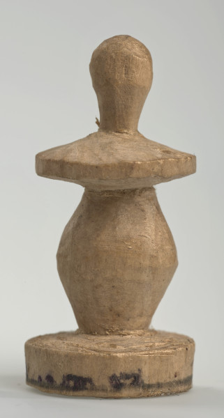 Ujęcie z boku [3]. Ze względu na swój okrągły kształt kolejne ujęcia z boku nie różnią się między sobą znacząco. Pionek został wykonany ręcznie z jednego kawałka jasnego drewna. Na całej powierzchni widoczne są ślady rzeźbienia przy pomocy noża. Obiekt w kolorze naturalnego drewna (nie został pomalowany, ani polakierowany). Krawędź podstawy została dodatkowo obrysowana ołówkiem. Pionek składa się ze spłaszczonej podstawy w formie krążka, części środkowej w kształcie gruszki, spłaszczonego ronda, które zwęża się stopniowo ku górze oraz ku dołowi (przypominając dwa połączone ze sobą talerze, z których każdy skierowany jest dnem do zewnątrz) oraz zwieńczenia o prostej, rozszerzającej się ku górze formie (przypominającej pałkę).