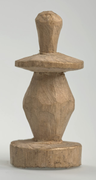 Ujęcie z boku [3]. Ze względu na swój okrągły kształt kolejne ujęcia z boku nie różnią się między sobą znacząco. Pionek został wykonany ręcznie z jednego kawałka jasnego drewna. Na całej powierzchni widoczne są ślady rzeźbienia przy pomocy noża. Obiekt w kolorze naturalnego drewna (nie został pomalowany, ani polakierowany). Od spodu widoczne oznaczenie składające się z dwóch przecinających się ze sobą linii („X”), które umożliwia podzielenie bierek pomiędzy dwóch graczy - wszystkie bierki są jednakowego koloru. Krawędź podstawy została dodatkowo obrysowana ołówkiem. Pionek składa się ze spłaszczonej podstawy w formie krążka, części środkowej w kształcie gruszki, spłaszczonego ronda, które zwęża się stopniowo ku górze oraz ku dołowi (przypominając dwa połączone ze sobą talerze, z których każdy skierowany jest dnem do zewnątrz) oraz zwieńczenia o prostej, rozszerzającej się ku górze formie (przypominającej pałkę).