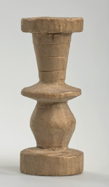 Ujęcie z boku [1]. Ze względu na swój okrągły kształt kolejne ujęcia z boku nie różnią się między sobą znacząco. Wieża została wykonana ręcznie z jednego kawałka jasnego drewna. Na całej powierzchni widoczne są ślady rzeźbienia przy pomocy noża. Obiekt w kolorze naturalnego drewna (nie został pomalowany, ani polakierowany). Od spodu widoczne oznaczenie składające się z dwóch przecinających się ze sobą linii („X”), które umożliwia podzielenie bierek pomiędzy dwóch graczy - wszystkie bierki są jednakowego koloru. Wieża składa się ze spłaszczonej podstawy w formie krążka, środkowej części w formie walca szerszego po środku, spłaszczonego cylindrycznego elementu, który zwęża się stopniowo ku górze oraz ku dołowi (przypominając dwa połączone ze sobą talerze, z których każdy skierowany jest dnem do zewnątrz) oraz zwieńczenia w kształcie kielicha, ozdobionego przy pomocy linii (żłobień).