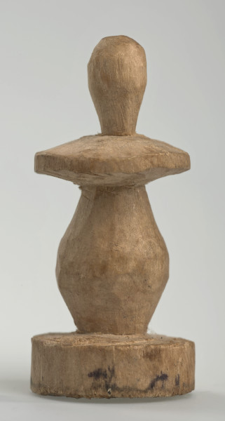 Ujęcie z boku [1]. Ze względu na swój okrągły kształt kolejne ujęcia z boku nie różnią się między sobą znacząco. Pionek został wykonany ręcznie z jednego kawałka jasnego drewna. Na całej powierzchni widoczne są ślady rzeźbienia przy pomocy noża. Obiekt w kolorze naturalnego drewna (nie został pomalowany, ani polakierowany). Krawędź podstawy została dodatkowo obrysowana ołówkiem. Pionek składa się ze spłaszczonej podstawy w formie krążka, części środkowej w kształcie gruszki, spłaszczonego ronda, które zwęża się stopniowo ku górze oraz ku dołowi (przypominając dwa połączone ze sobą talerze, z których każdy skierowany jest dnem do zewnątrz) oraz zwieńczenia o prostej, rozszerzającej się ku górze formie (przypominającej pałkę).