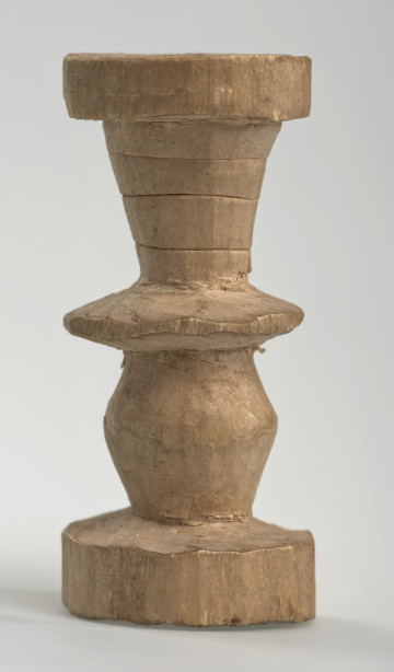 Ujęcie z boku [1]. Ze względu na swój okrągły kształt kolejne ujęcia z boku nie różnią się między sobą znacząco. Wieża została wykonana ręcznie z jednego kawałka jasnego drewna. Na całej powierzchni widoczne są ślady rzeźbienia przy pomocy noża. Obiekt w kolorze naturalnego drewna (nie został pomalowany, ani polakierowany). Od spodu widoczne oznaczenie składające się z dwóch przecinających się ze sobą linii („X”), które umożliwia podzielenie bierek pomiędzy dwóch graczy - wszystkie bierki są jednakowego koloru. Wieża składa się ze spłaszczonej podstawy w formie krążka, środkowej części w formie walca szerszego po środku, spłaszczonego cylindrycznego elementu, który zwęża się stopniowo ku górze oraz ku dołowi (przypominając dwa połączone ze sobą talerze, z których każdy skierowany jest dnem do zewnątrz) oraz zwieńczenia w kształcie kielicha, ozdobionego przy pomocy linii (żłobień).