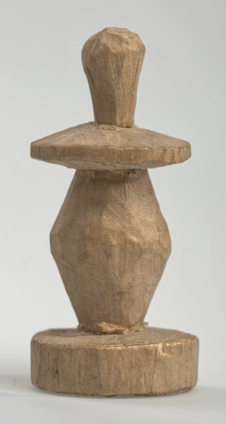 Ujęcie z boku [1]. Ze względu na swój okrągły kształt kolejne ujęcia z boku nie różnią się między sobą znacząco. Pionek został wykonany ręcznie z jednego kawałka jasnego drewna. Na całej powierzchni widoczne są ślady rzeźbienia przy pomocy noża. Obiekt w kolorze naturalnego drewna (nie został pomalowany, ani polakierowany). Od spodu widoczne oznaczenie składające się z dwóch przecinających się ze sobą linii („X”), które umożliwia podzielenie bierek pomiędzy dwóch graczy - wszystkie bierki są jednakowego koloru. Krawędź podstawy została dodatkowo obrysowana ołówkiem. Pionek składa się ze spłaszczonej podstawy w formie krążka, części środkowej w kształcie gruszki, spłaszczonego ronda, które zwęża się stopniowo ku górze oraz ku dołowi (przypominając dwa połączone ze sobą talerze, z których każdy skierowany jest dnem do zewnątrz) oraz zwieńczenia o prostej, rozszerzającej się ku górze formie (przypominającej pałkę).