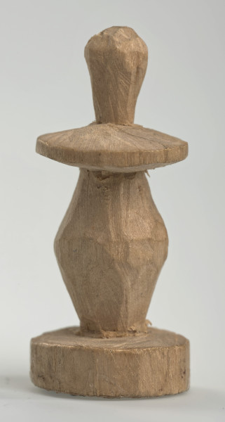 Ujęcie z boku [4]. Ze względu na swój okrągły kształt kolejne ujęcia z boku nie różnią się między sobą znacząco. Pionek został wykonany ręcznie z jednego kawałka jasnego drewna. Na całej powierzchni widoczne są ślady rzeźbienia przy pomocy noża. Obiekt w kolorze naturalnego drewna (nie został pomalowany, ani polakierowany). Od spodu widoczne oznaczenie składające się z dwóch przecinających się ze sobą linii („X”), które umożliwia podzielenie bierek pomiędzy dwóch graczy - wszystkie bierki są jednakowego koloru. Krawędź podstawy została dodatkowo obrysowana ołówkiem. Pionek składa się ze spłaszczonej podstawy w formie krążka, części środkowej w kształcie gruszki, spłaszczonego ronda, które zwęża się stopniowo ku górze oraz ku dołowi (przypominając dwa połączone ze sobą talerze, z których każdy skierowany jest dnem do zewnątrz) oraz zwieńczenia o prostej, rozszerzającej się ku górze formie (przypominającej pałkę).