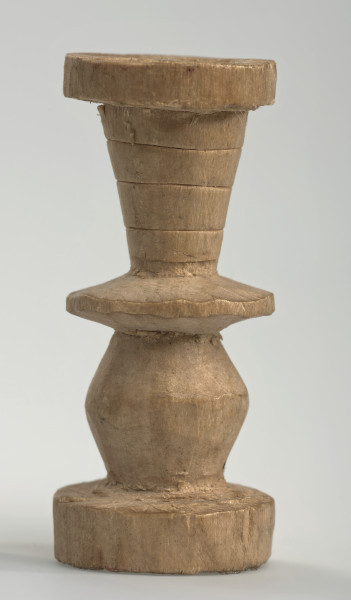 Ujęcie z boku [2]. Ze względu na swój okrągły kształt kolejne ujęcia z boku nie różnią się między sobą znacząco. Wieża została wykonana ręcznie z jednego kawałka jasnego drewna. Na całej powierzchni widoczne są ślady rzeźbienia przy pomocy noża. Obiekt w kolorze naturalnego drewna (nie został pomalowany, ani polakierowany). Od spodu widoczne oznaczenie składające się z dwóch przecinających się ze sobą linii („X”), które umożliwia podzielenie bierek pomiędzy dwóch graczy - wszystkie bierki są jednakowego koloru. Wieża składa się ze spłaszczonej podstawy w formie krążka, środkowej części w formie walca szerszego po środku, spłaszczonego cylindrycznego elementu, który zwęża się stopniowo ku górze oraz ku dołowi (przypominając dwa połączone ze sobą talerze, z których każdy skierowany jest dnem do zewnątrz) oraz zwieńczenia w kształcie kielicha, ozdobionego przy pomocy linii (żłobień).