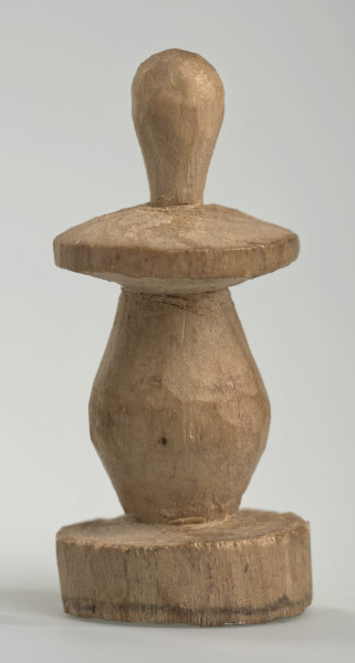 Ujęcie z boku [3]. Ze względu na swój okrągły kształt kolejne ujęcia z boku nie różnią się między sobą znacząco. Pionek został wykonany ręcznie z jednego kawałka jasnego drewna. Na całej powierzchni widoczne są ślady rzeźbienia przy pomocy noża. Obiekt w kolorze naturalnego drewna (nie został pomalowany, ani polakierowany). Krawędź podstawy została dodatkowo obrysowana ołówkiem. Pionek składa się ze spłaszczonej podstawy w formie krążka, części środkowej w kształcie gruszki, spłaszczonego ronda, które zwęża się stopniowo ku górze oraz ku dołowi (przypominając dwa połączone ze sobą talerze, z których każdy skierowany jest dnem do zewnątrz) oraz zwieńczenia o prostej, rozszerzającej się ku górze formie (przypominającej pałkę).