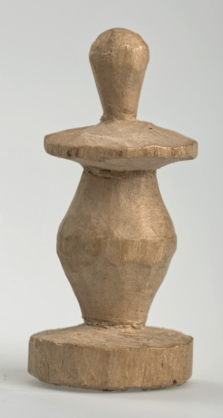 Ujęcie z boku [2]. Ze względu na swój okrągły kształt kolejne ujęcia z boku nie różnią się między sobą znacząco. Pionek został wykonany ręcznie z jednego kawałka jasnego drewna. Na całej powierzchni widoczne są ślady rzeźbienia przy pomocy noża. Obiekt w kolorze naturalnego drewna (nie został pomalowany, ani polakierowany). Od spodu widoczne oznaczenie składające się z dwóch przecinających się ze sobą linii („X”), które umożliwia podzielenie bierek pomiędzy dwóch graczy - wszystkie bierki są jednakowego koloru. Krawędź podstawy została dodatkowo obrysowana ołówkiem. Pionek składa się ze spłaszczonej podstawy w formie krążka, części środkowej w kształcie gruszki, spłaszczonego ronda, które zwęża się stopniowo ku górze oraz ku dołowi (przypominając dwa połączone ze sobą talerze, z których każdy skierowany jest dnem do zewnątrz) oraz zwieńczenia o prostej, rozszerzającej się ku górze formie (przypominającej pałkę).