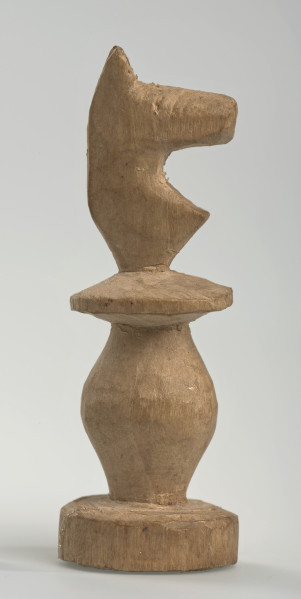 Ujęcie prawego boku. 
Skoczek został wykonany ręcznie z jednego kawałka jasnego drewna. Na całej powierzchni widoczne są ślady rzeźbienia przy pomocy noża. Obiekt w kolorze naturalnego drewna (nie został pomalowany, ani polakierowany). Od spodu widoczne oznaczenie składające się z dwóch przecinających się ze sobą linii („X”), które umożliwia podzielenie bierek pomiędzy dwóch graczy - wszystkie bierki są jednakowego koloru. Skoczek składa się ze spłaszczonej podstawy w formie krążka, części środkowej w formie walca rozszerzającego się po środku wysokości, spłaszczonego cylindrycznego elementu, który zwęża się stopniowo ku górze oraz ku dołowi (przypominając dwa połączone ze sobą talerze, z których każdy skierowany jest dnem do zewnątrz) oraz zwieńczenia w formie nawiązującej do głowy i szyi konia. Głowa oraz szyja są spłaszczone. Widoczne wyżłobione oko.