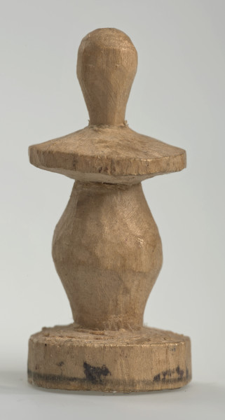 Ujęcie z boku [4]. Ze względu na swój okrągły kształt kolejne ujęcia z boku nie różnią się między sobą znacząco. Pionek został wykonany ręcznie z jednego kawałka jasnego drewna. Na całej powierzchni widoczne są ślady rzeźbienia przy pomocy noża. Obiekt w kolorze naturalnego drewna (nie został pomalowany, ani polakierowany). Krawędź podstawy została dodatkowo obrysowana ołówkiem. Pionek składa się ze spłaszczonej podstawy w formie krążka, części środkowej w kształcie gruszki, spłaszczonego ronda, które zwęża się stopniowo ku górze oraz ku dołowi (przypominając dwa połączone ze sobą talerze, z których każdy skierowany jest dnem do zewnątrz) oraz zwieńczenia o prostej, rozszerzającej się ku górze formie (przypominającej pałkę).